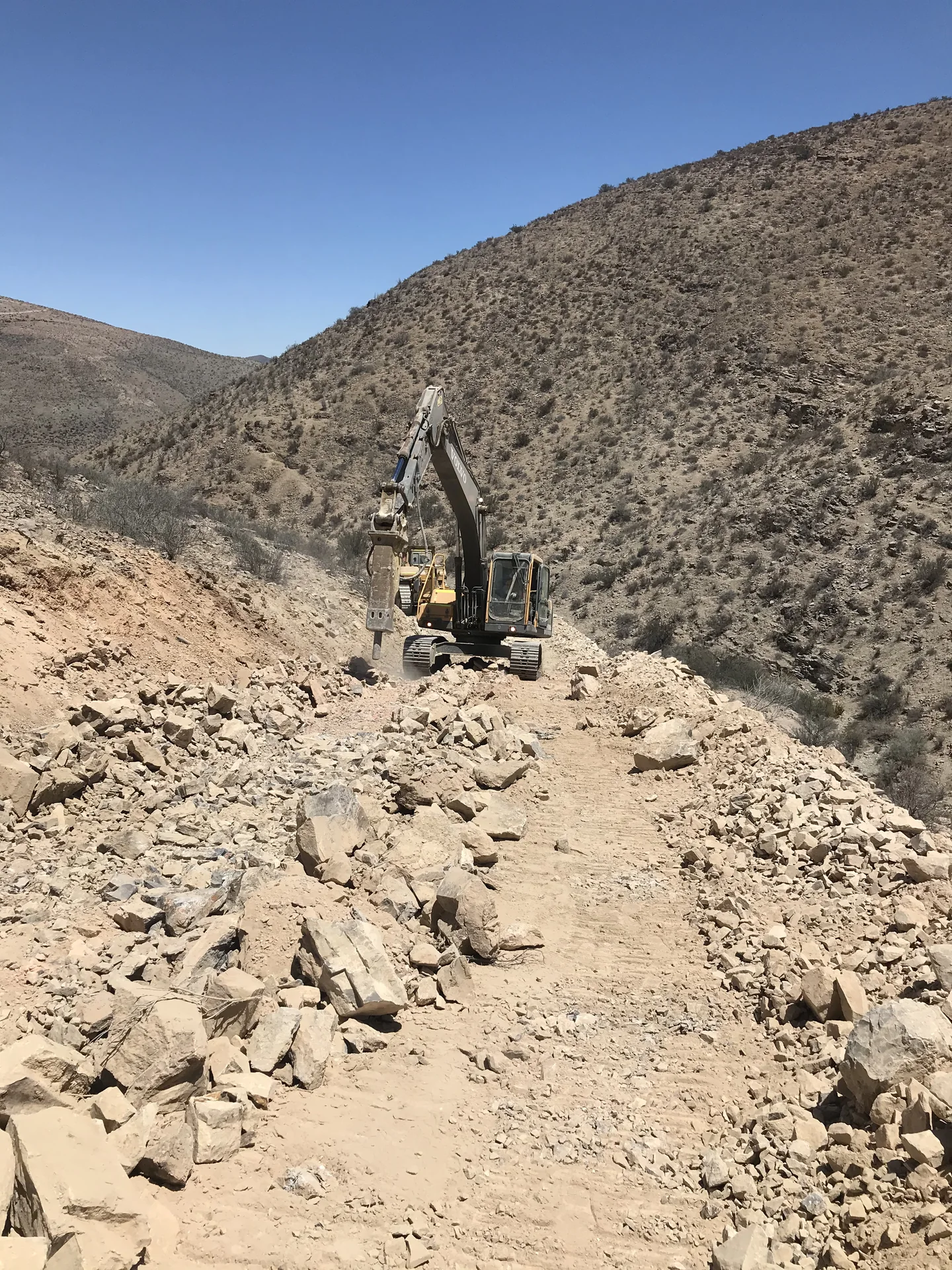 Excavadora QMT trabajando en la apertura de un camino entre cerros